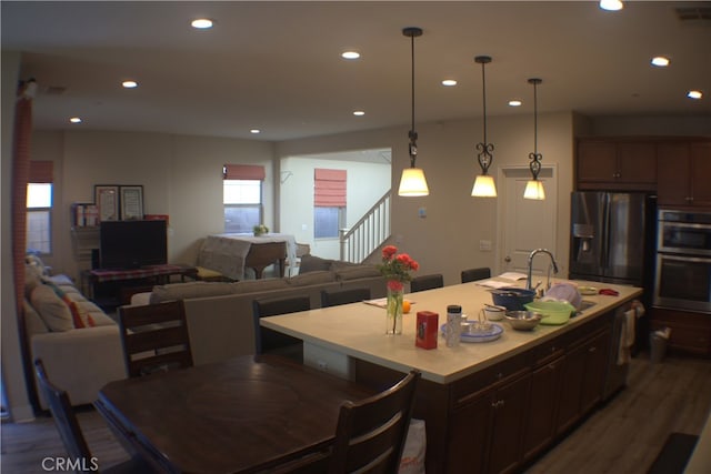 kitchen featuring appliances with stainless steel finishes, a kitchen island with sink, dark wood-type flooring, sink, and decorative light fixtures