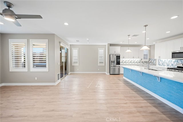 kitchen with a kitchen bar, appliances with stainless steel finishes, light wood-type flooring, pendant lighting, and white cabinets