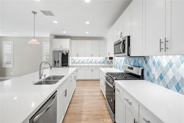 kitchen with pendant lighting, sink, light hardwood / wood-style floors, white cabinetry, and stainless steel appliances