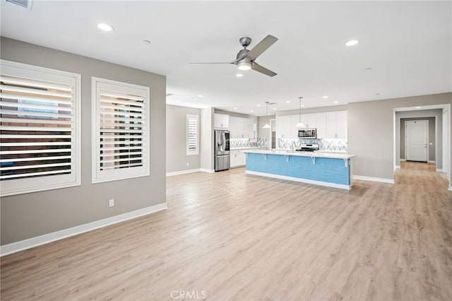 kitchen featuring white cabinetry, hanging light fixtures, light hardwood / wood-style flooring, a kitchen island with sink, and appliances with stainless steel finishes