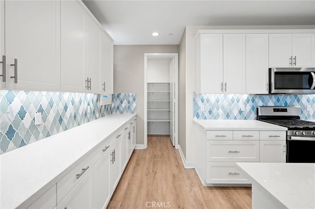 kitchen featuring white cabinets, decorative backsplash, light wood-type flooring, and stainless steel appliances