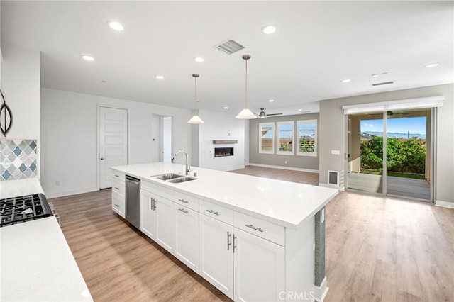 kitchen with dishwasher, sink, hanging light fixtures, an island with sink, and white cabinets