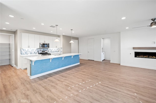 kitchen featuring sink, hanging light fixtures, light hardwood / wood-style flooring, appliances with stainless steel finishes, and white cabinetry