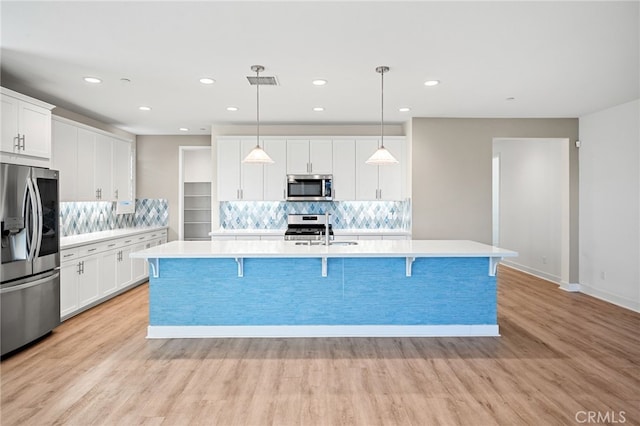 kitchen featuring an island with sink, pendant lighting, white cabinets, and stainless steel appliances