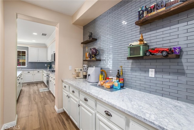 kitchen featuring light stone countertops, backsplash, light hardwood / wood-style floors, and white cabinetry