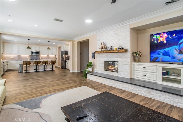 living room featuring crown molding, a stone fireplace, and dark hardwood / wood-style flooring