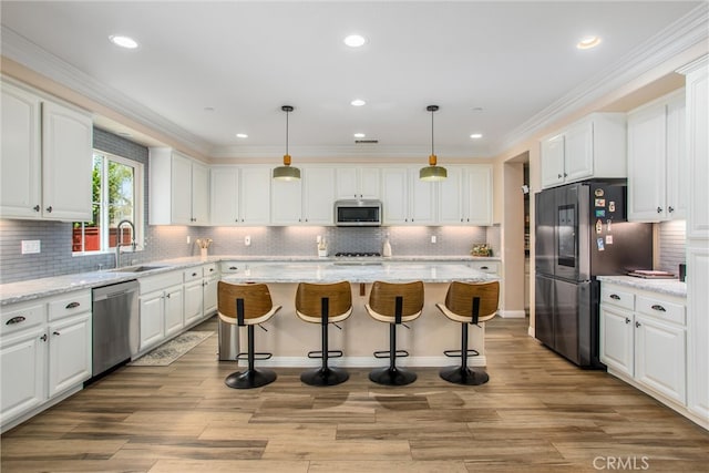 kitchen with a center island, sink, white cabinets, stainless steel appliances, and decorative light fixtures