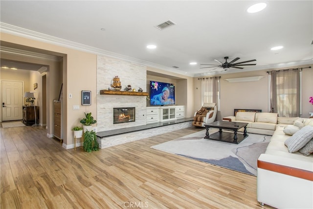 living room with ceiling fan, a stone fireplace, hardwood / wood-style flooring, and crown molding