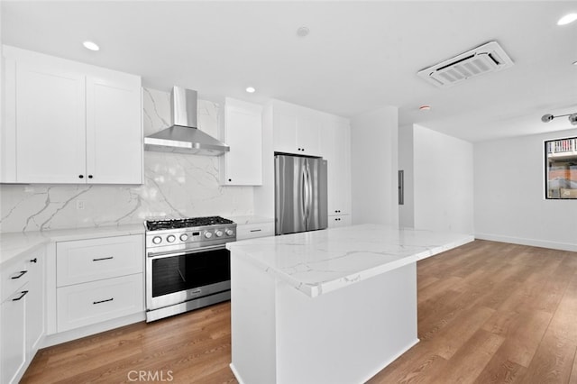 kitchen with white cabinets, a center island, appliances with stainless steel finishes, and wall chimney range hood