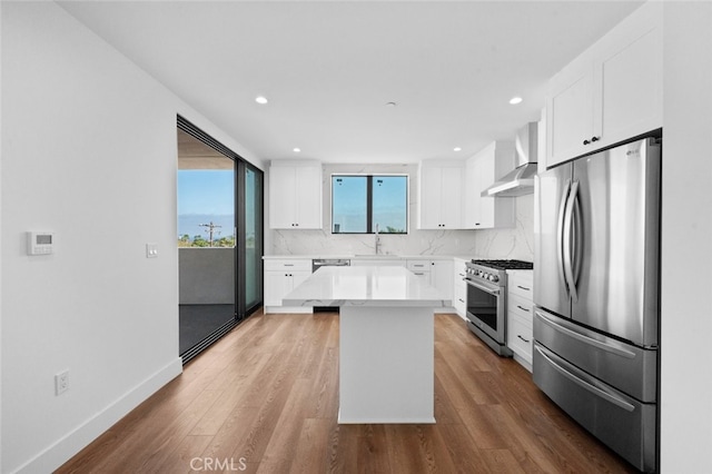 kitchen featuring white cabinets, wall chimney range hood, hardwood / wood-style flooring, stainless steel appliances, and a center island