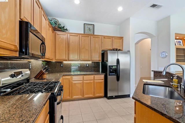 kitchen featuring light tile patterned floors, appliances with stainless steel finishes, decorative backsplash, dark stone counters, and sink