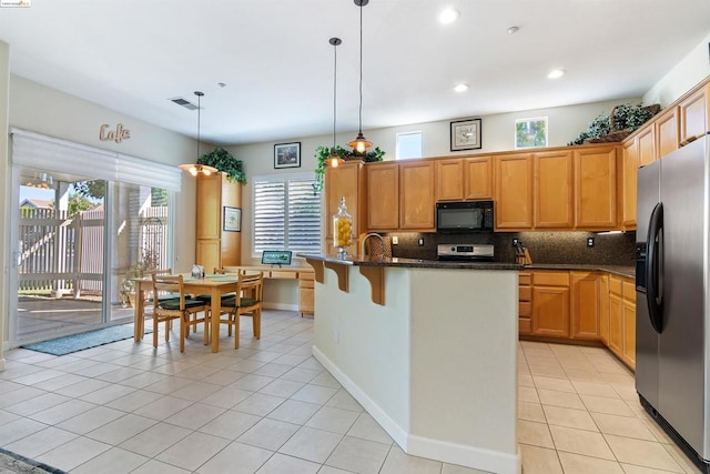 kitchen with dark stone countertops, hanging light fixtures, stainless steel fridge with ice dispenser, a kitchen island with sink, and light tile patterned floors