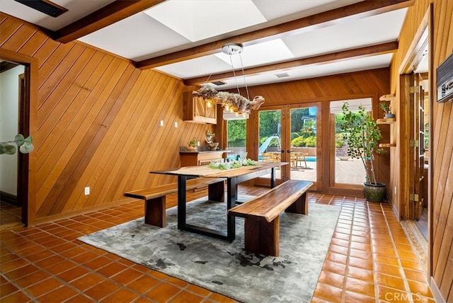 dining room featuring tile patterned flooring, beam ceiling, a skylight, french doors, and wooden walls