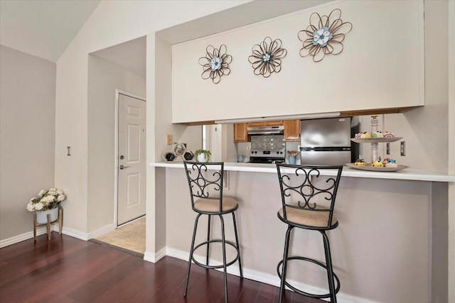 kitchen with dark hardwood / wood-style flooring, kitchen peninsula, a kitchen breakfast bar, stainless steel appliances, and vaulted ceiling