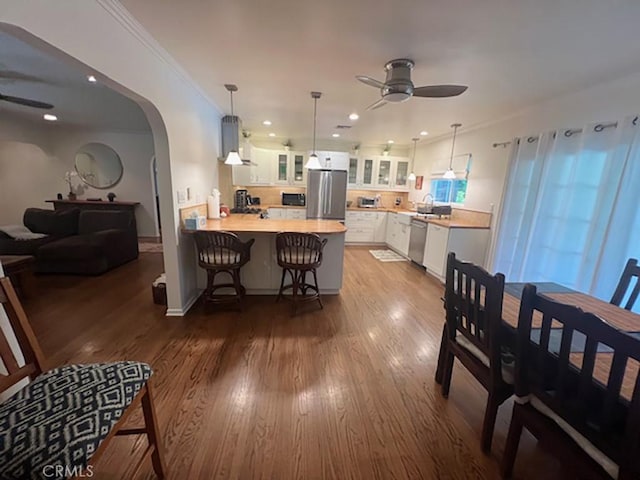 interior space with hardwood / wood-style floors, kitchen peninsula, ceiling fan, appliances with stainless steel finishes, and white cabinetry