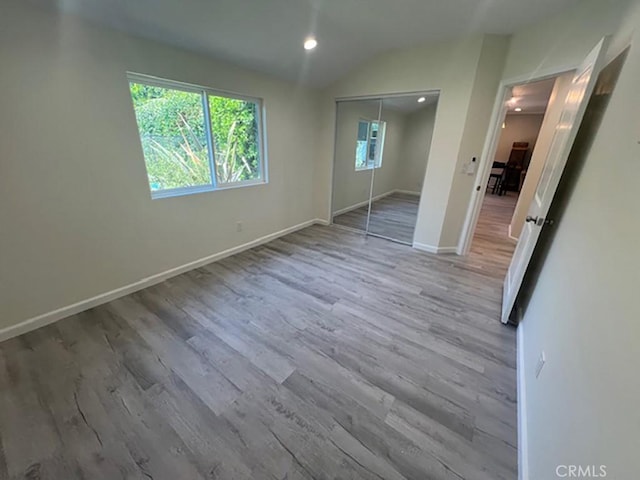 unfurnished bedroom featuring light hardwood / wood-style floors, lofted ceiling, and a closet