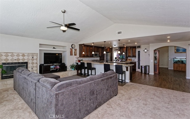 carpeted living room featuring ceiling fan, vaulted ceiling, and a fireplace