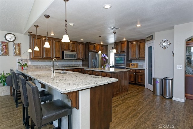 kitchen featuring dark wood-type flooring, kitchen peninsula, pendant lighting, appliances with stainless steel finishes, and a textured ceiling