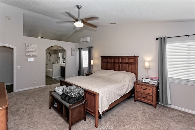 bedroom featuring an AC wall unit, ensuite bath, vaulted ceiling, light colored carpet, and ceiling fan