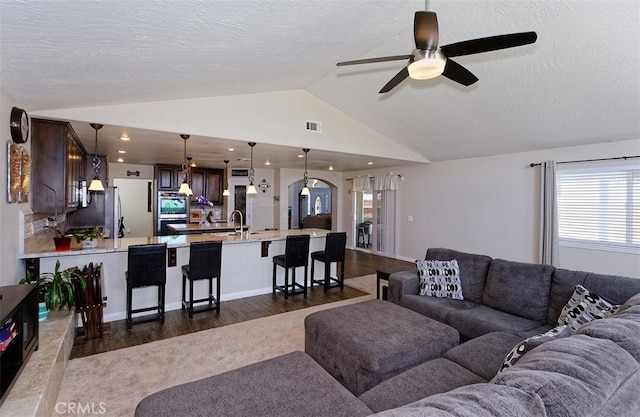 living room with sink, a textured ceiling, ceiling fan, vaulted ceiling, and dark wood-type flooring