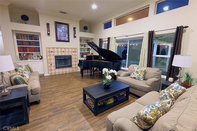 living room with a tiled fireplace, hardwood / wood-style flooring, crown molding, built in features, and a towering ceiling