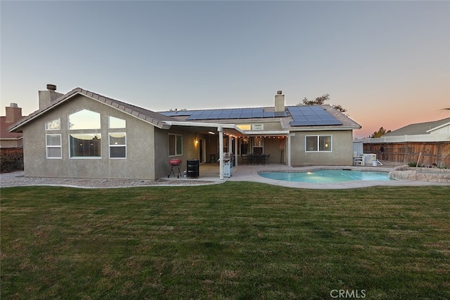 back house at dusk with a fenced in pool, a patio area, solar panels, and a lawn