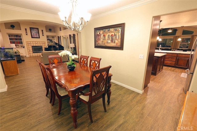 dining room with crown molding, a chandelier, a tile fireplace, and hardwood / wood-style floors