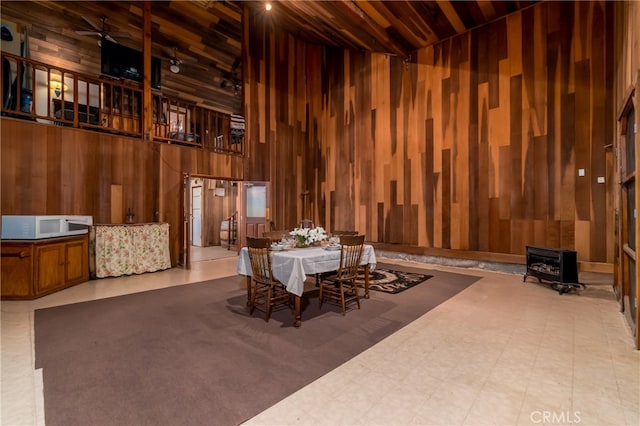 dining space featuring ceiling fan, wood ceiling, a wood stove, wooden walls, and high vaulted ceiling