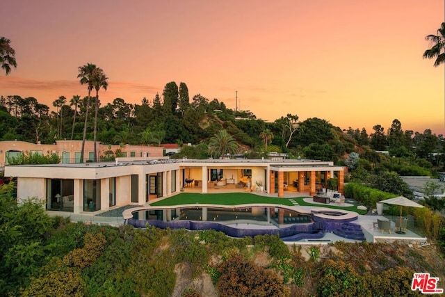 back house at dusk with a swimming pool with hot tub and a patio area