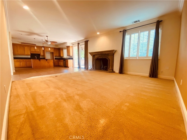 unfurnished living room featuring ornamental molding, ceiling fan, light colored carpet, and plenty of natural light