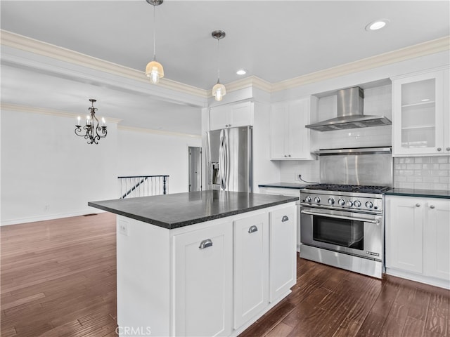 kitchen with tasteful backsplash, white cabinets, wall chimney exhaust hood, stainless steel appliances, and decorative light fixtures