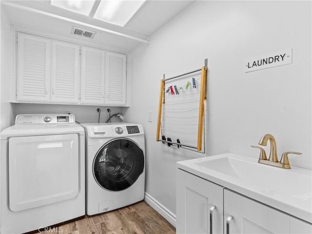 clothes washing area with hardwood / wood-style floors, washing machine and clothes dryer, sink, and cabinets