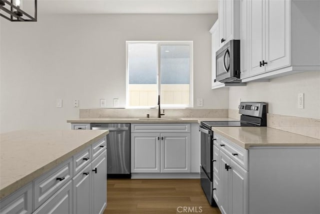 kitchen with appliances with stainless steel finishes, dark hardwood / wood-style flooring, white cabinetry, and sink