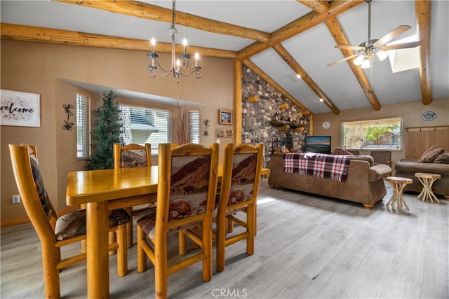 dining area with light hardwood / wood-style floors, high vaulted ceiling, ceiling fan with notable chandelier, a stone fireplace, and beamed ceiling