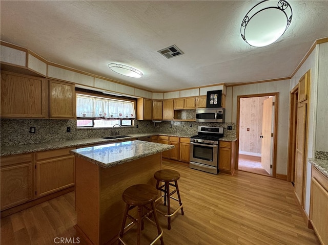 kitchen featuring stainless steel appliances, a center island, light wood-type flooring, and sink