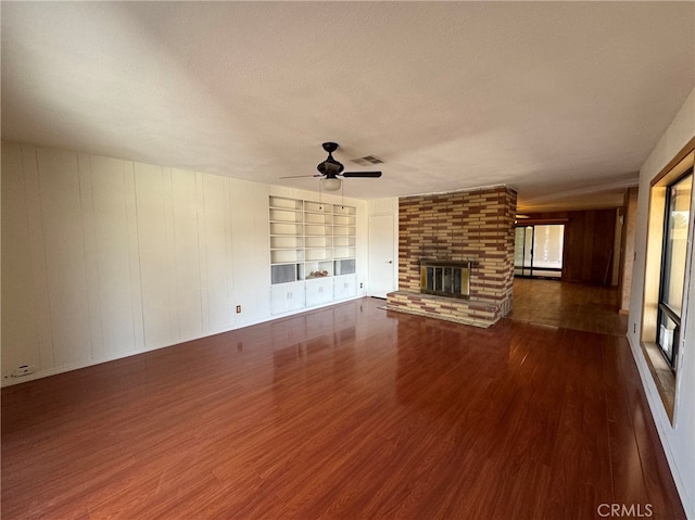 unfurnished living room with a healthy amount of sunlight, a brick fireplace, ceiling fan, and dark wood-type flooring