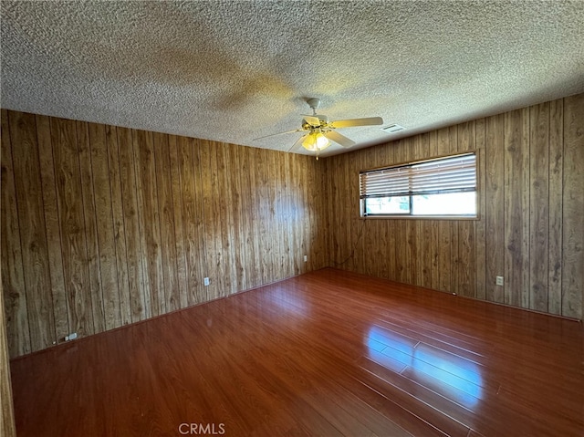 empty room with wooden walls, ceiling fan, hardwood / wood-style flooring, and a textured ceiling