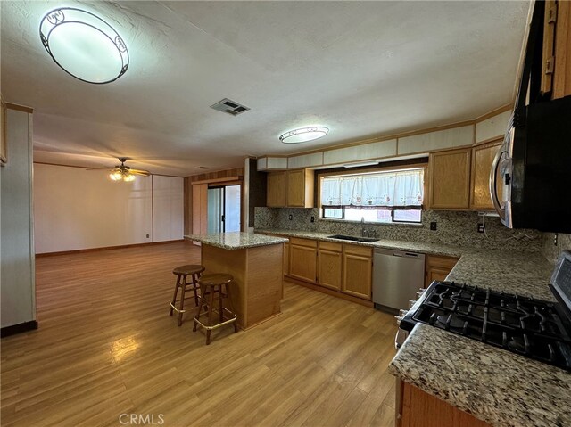 kitchen featuring light wood-type flooring, sink, a kitchen island, a kitchen breakfast bar, and appliances with stainless steel finishes