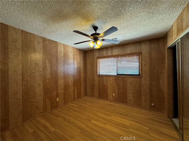 spare room with wood walls, light hardwood / wood-style floors, ceiling fan, and a textured ceiling