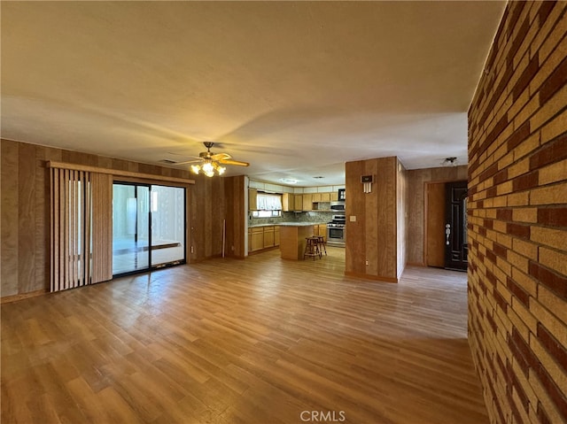 unfurnished living room featuring light wood-type flooring, wooden walls, and ceiling fan