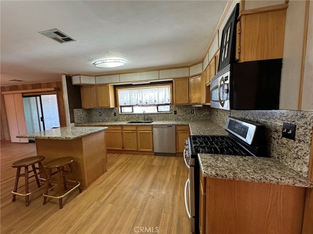 kitchen featuring light stone counters, light hardwood / wood-style flooring, stainless steel appliances, a center island, and a breakfast bar area