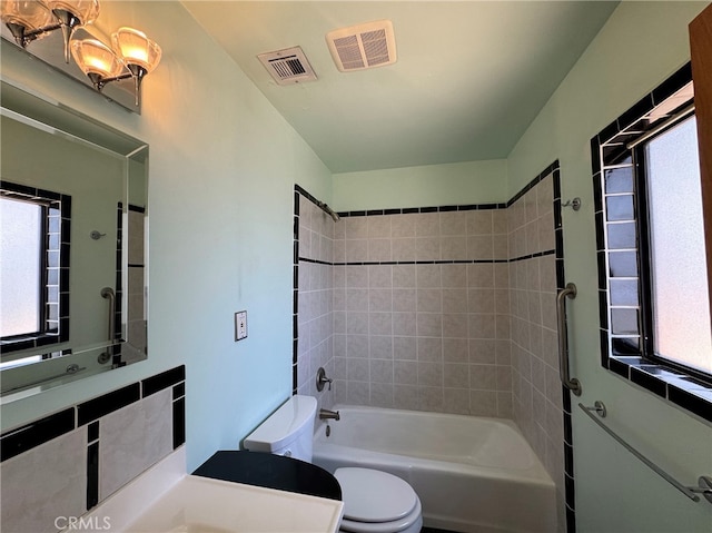 bathroom with an inviting chandelier, toilet, and tiled shower / bath