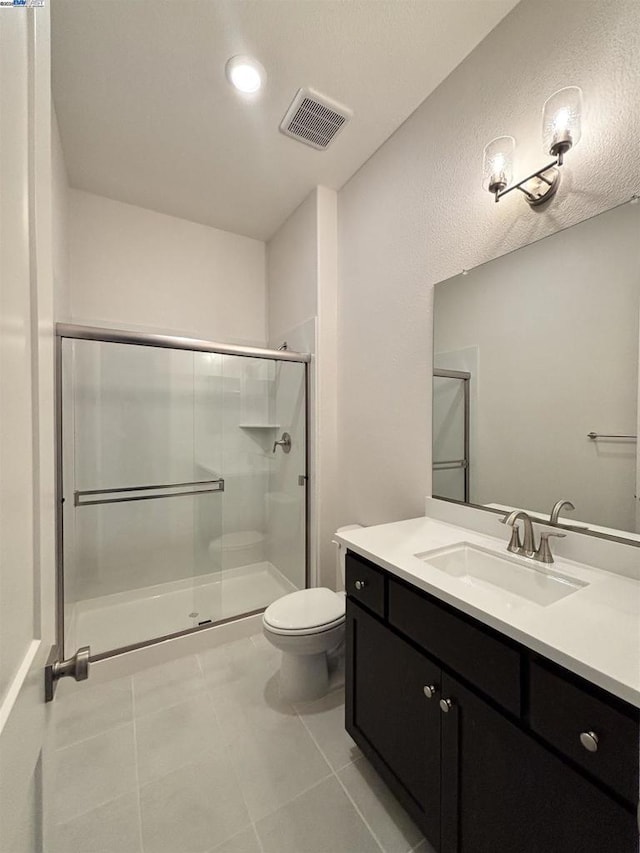 bathroom with a shower with door, tile patterned flooring, vanity, and toilet