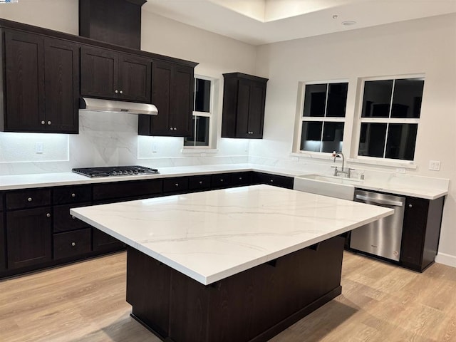 kitchen with sink, light stone counters, light hardwood / wood-style flooring, a kitchen island, and appliances with stainless steel finishes