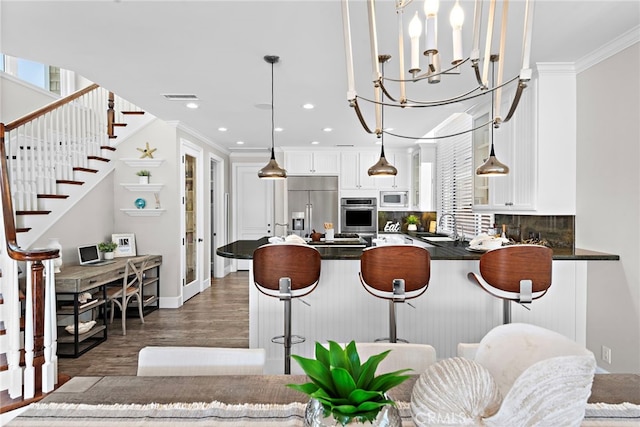 kitchen featuring dark wood-type flooring, white cabinetry, built in appliances, hanging light fixtures, and a breakfast bar area