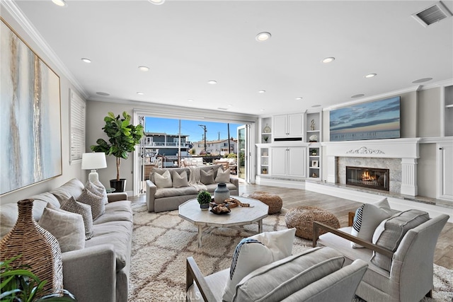 living room with light hardwood / wood-style floors, built in shelves, a high end fireplace, and ornamental molding