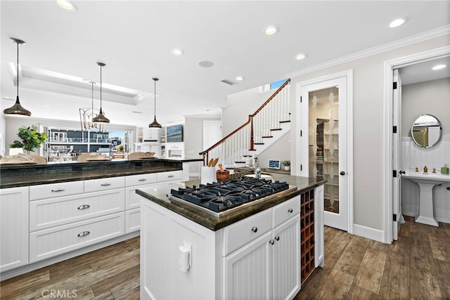 kitchen featuring stainless steel gas stovetop, dark wood-type flooring, pendant lighting, white cabinets, and a center island