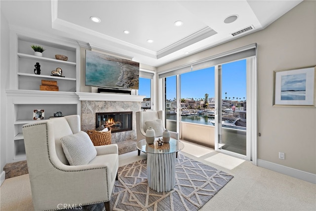 living room featuring built in features, a fireplace, a tray ceiling, and ornamental molding