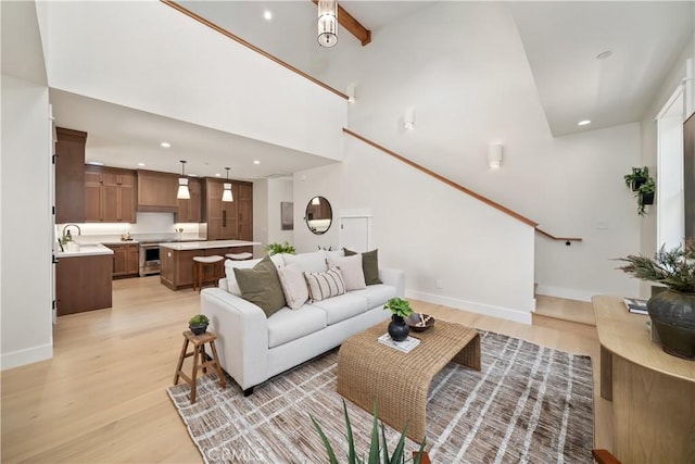 living room featuring a towering ceiling, sink, beam ceiling, and light hardwood / wood-style flooring