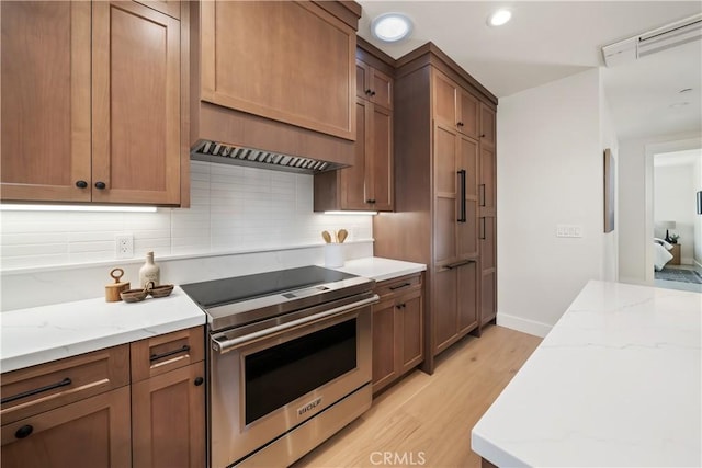 kitchen featuring light stone counters, stainless steel range with electric stovetop, light hardwood / wood-style floors, and decorative backsplash